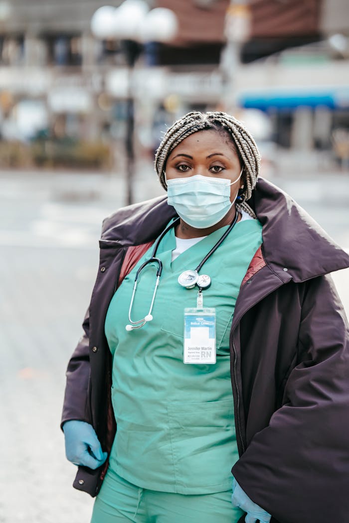 African American woman doctor in medical mask and uniform standing on street in city and looking at camera