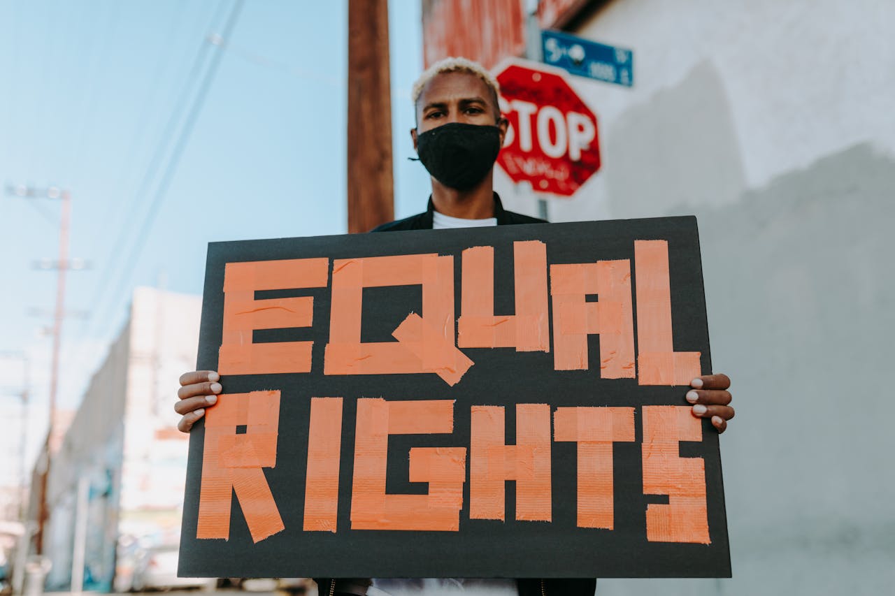 Person in mask holding 'Equal Rights' sign at a protest outdoors.