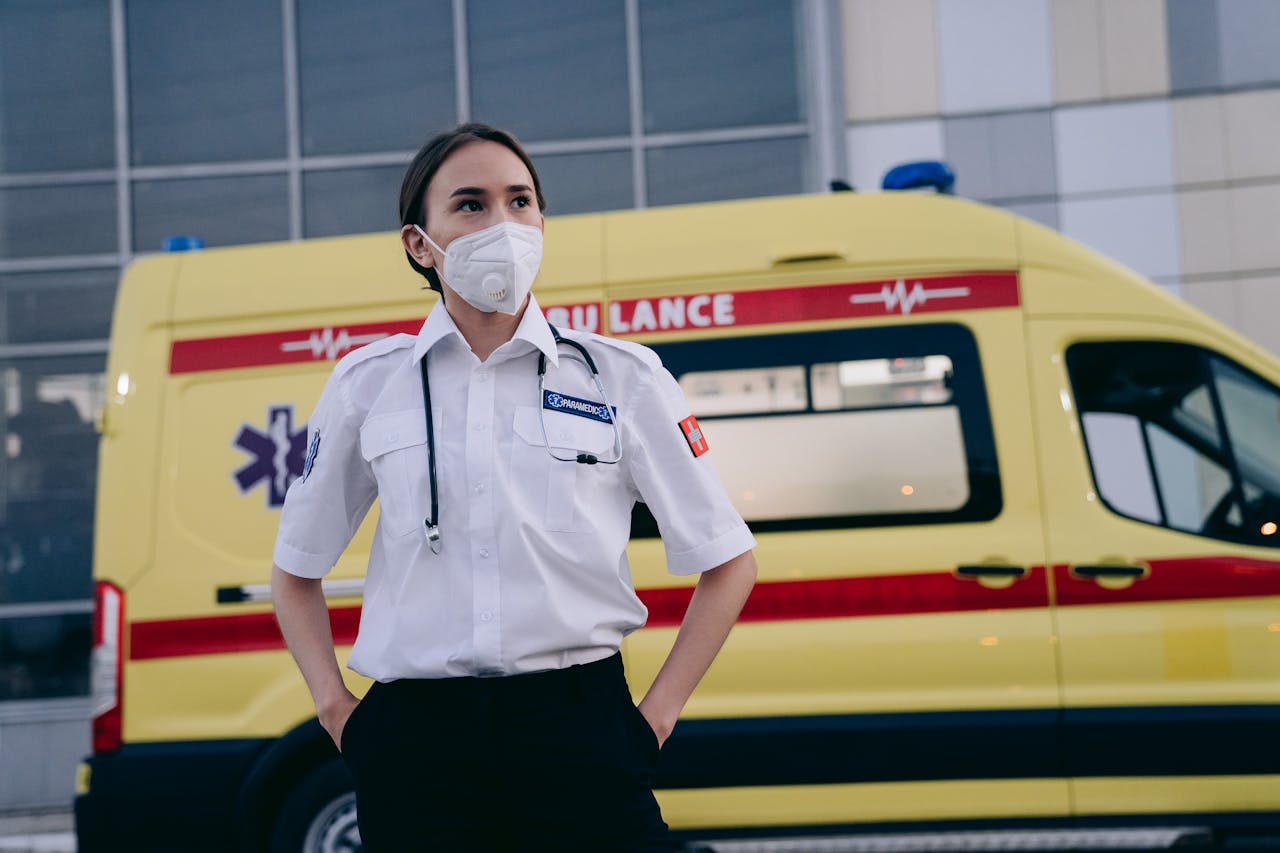 A paramedic with a face mask standing confidently beside an ambulance vehicle.